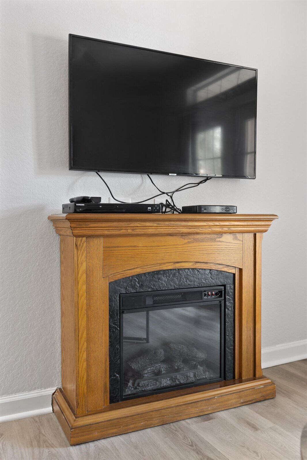 A flat-screen TV mounted on a wall above a wooden fireplace with a glass door.