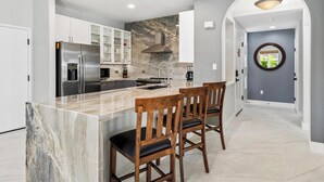 Una cocina moderna con una isla de mármol, electrodomésticos de acero inoxidable y taburetes de madera.