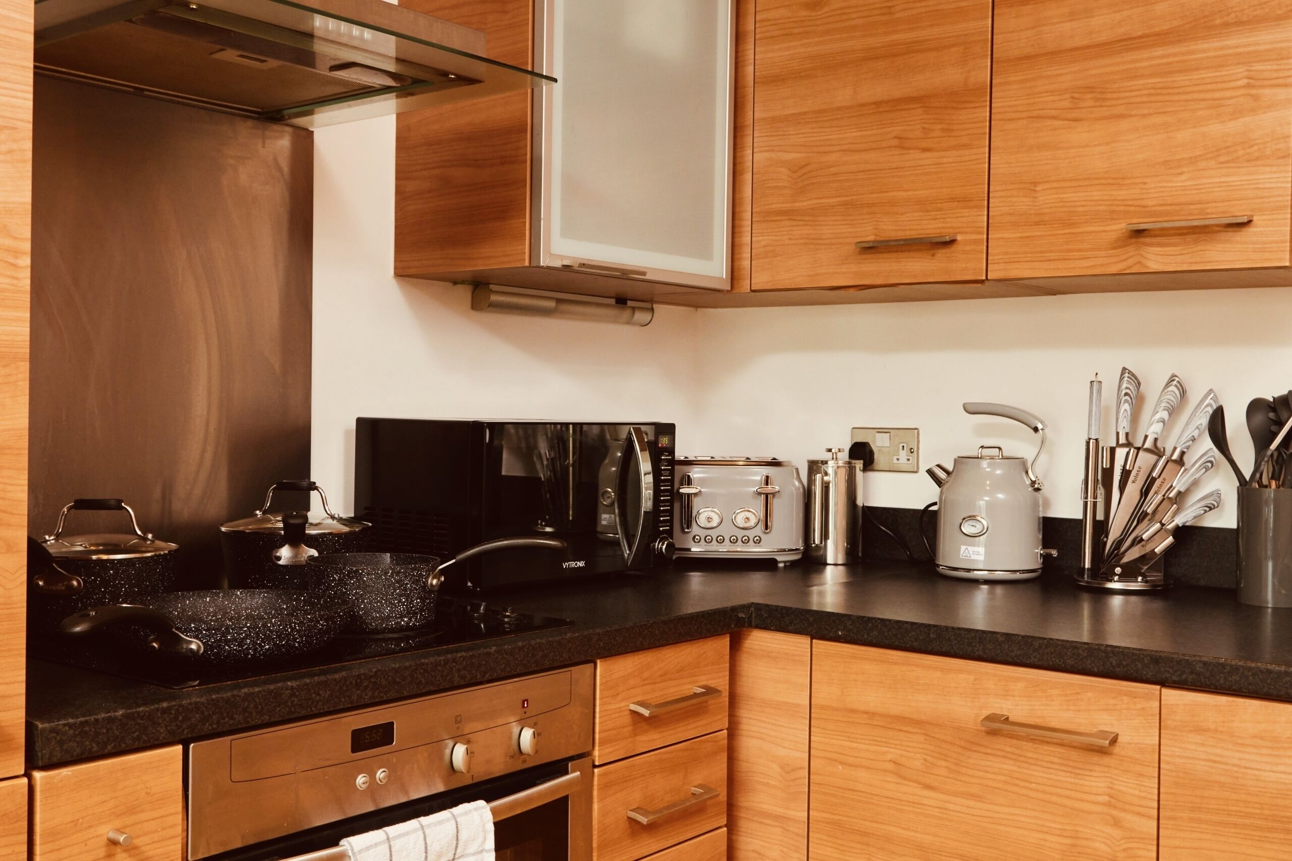 A kitchen with wooden cabinets, a black countertop, a stove, a microwave, a toaster, and a kettle.