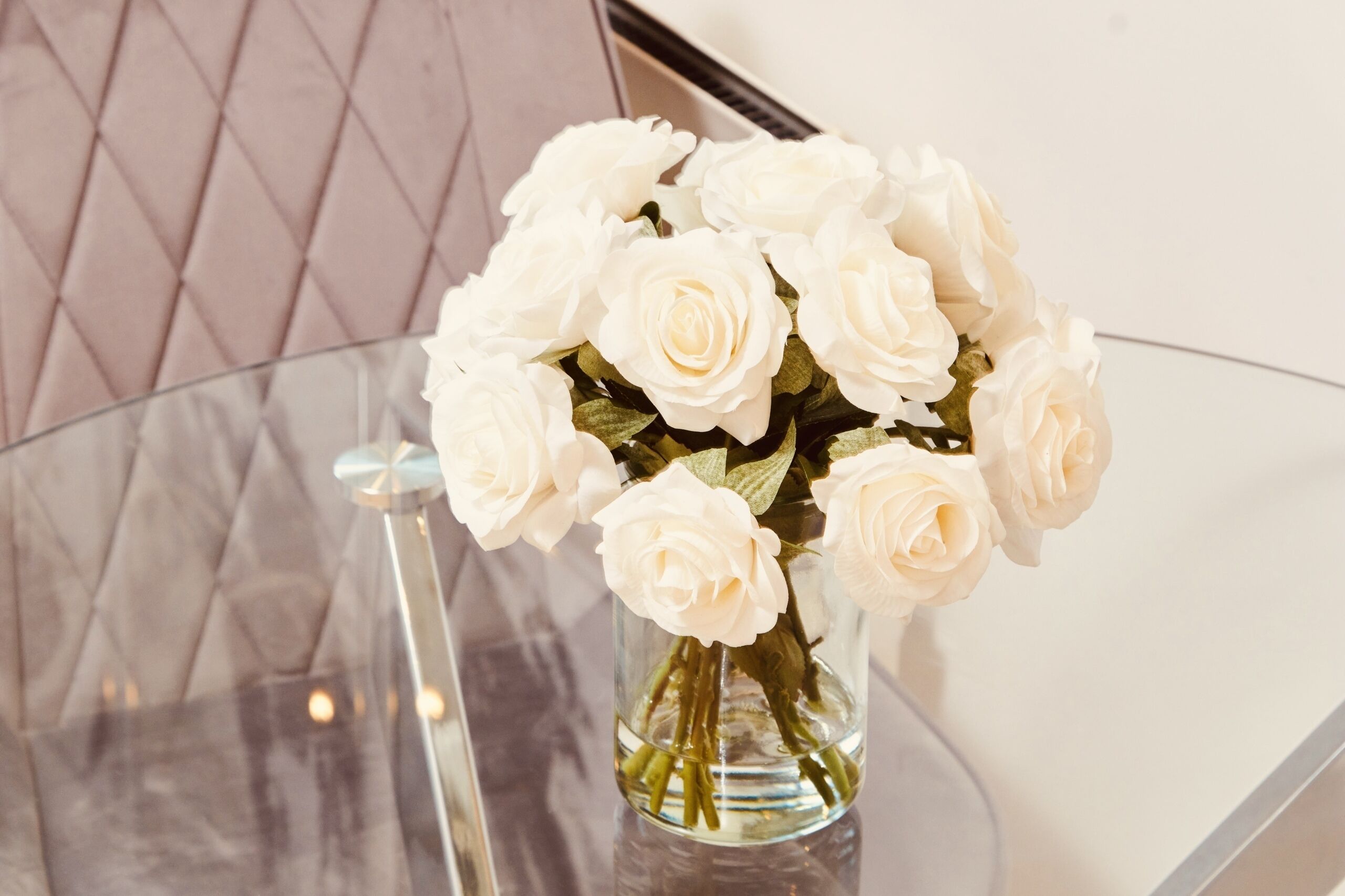 Un florero de cristal transparente con rosas blancas sobre una mesa de cristal.
