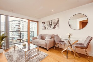 A modern living room with a glass coffee table, a beige sofa, and a round mirror. - Deluxe City Apt, Beautiful River View&free Parking (Leeds)