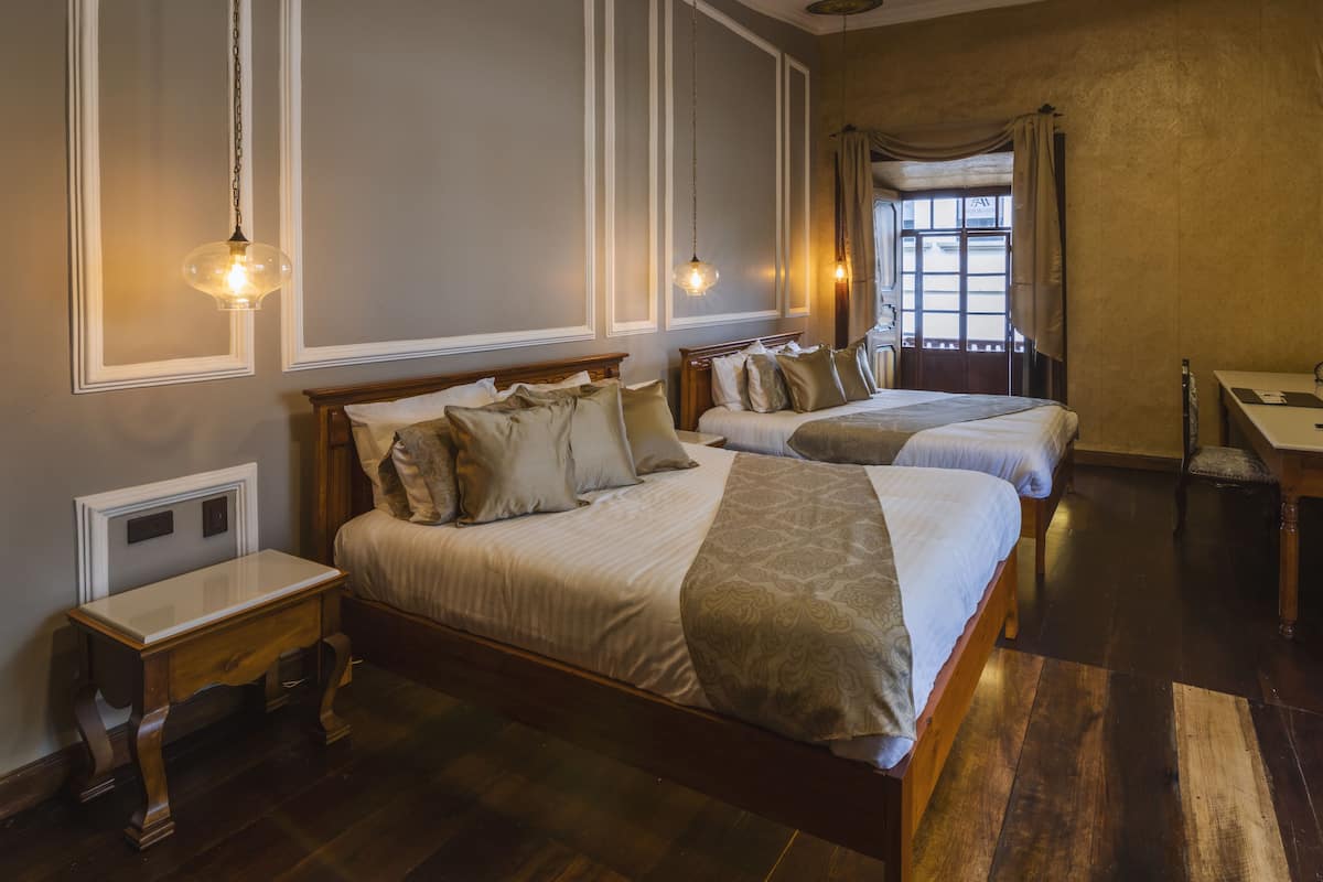 A hotel room with two beds, a wooden nightstand, a desk, and a window with curtains.