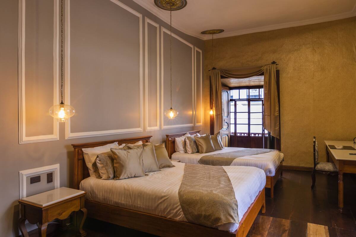 A bedroom with two beds, wooden flooring, and a desk.