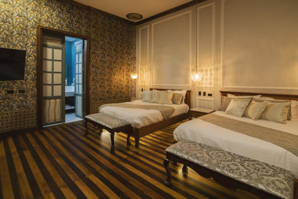 A hotel room with two beds, a wooden floor, a stone wall, and a television on the wall.