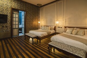 Habitación de hotel con dos camas, suelo de madera, pared de piedra y televisor en la pared.