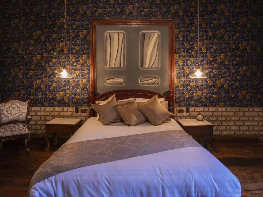 Een slaapkamer met een groot bed, twee nachtkastjes, een houten stoel en een behang met een patroon.