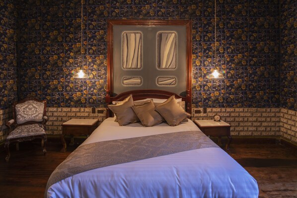 Un dormitorio con una cama grande, dos mesitas de noche, una silla de madera y un papel tapiz estampado.