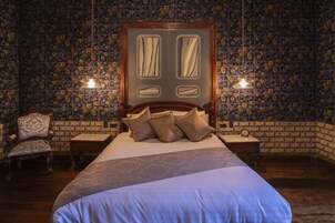 Un dormitorio con una cama grande, dos mesitas de noche, una silla de madera y un papel tapiz estampado.