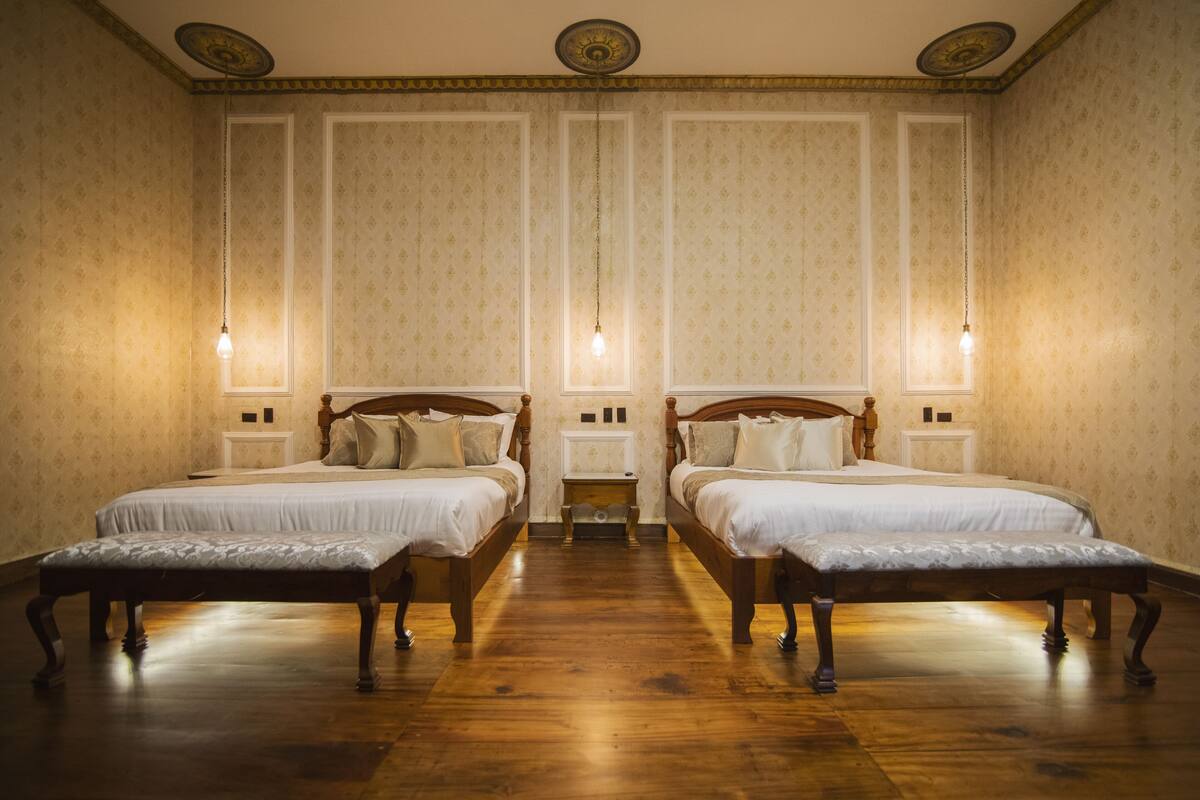 A room with two wooden beds, a bench, and a small table between them.