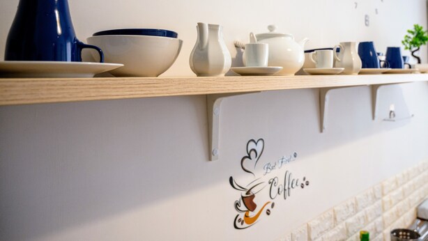 A kitchen counter with various tea and coffee items, including a blue teapot, white cups, and a teapot on a shelf.