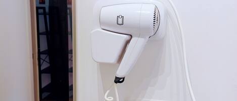 Ein weißer Haartrockner an einer Wand montiert, mit Steckdose und aufgewickeltem Kabel.