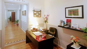 A reception area with a desk, chair, and a 'HOME' sign on the wall. There are potted plants, a framed picture, and a small shelf with books and a sign. - El Dorado Prati (Rome)