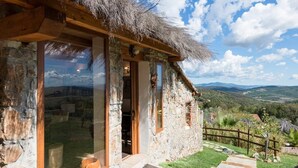 Uma casa de pedra com telhado de palha, janelas grandes e vista para o campo.