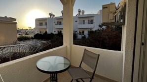 A balcony with a glass table and chairs, overlooking a residential area with buildings and a clear sky.