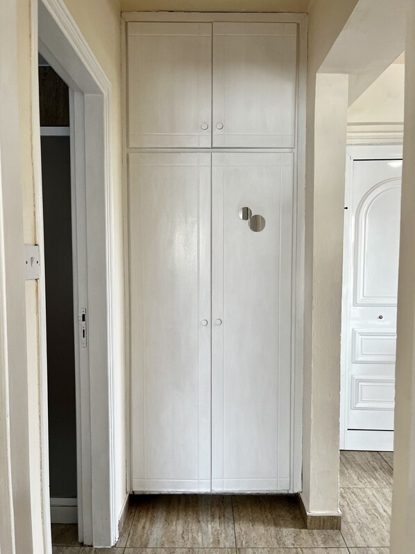 A white wardrobe with two doors and a small circular handle, located in a hallway with tiled flooring. - STAY Chill n' Joy (Ayia Napa)