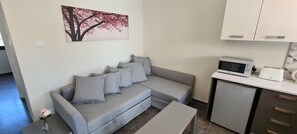 Una sala moderna con un sofá gris, una mesita, un microondas y un tostador sobre una encimera blanca.