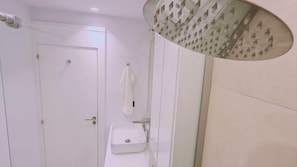 Uma casa de banho moderna com uma pia branca, uma toalha pendurada na parede e um chuveiro com um design de teto exclusivo.