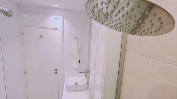 A modern bathroom with a white sink, a towel hanging on the wall, and a shower with a unique ceiling design.