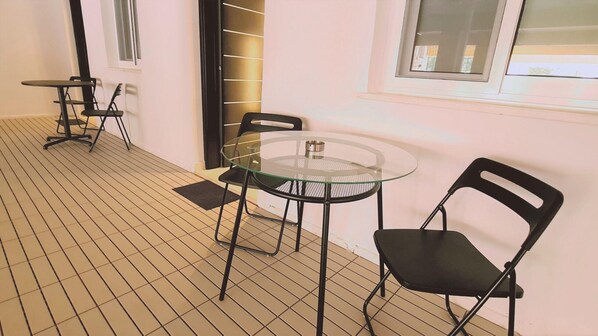 A room with a tiled floor, a round glass table with two chairs, and a window with blinds.