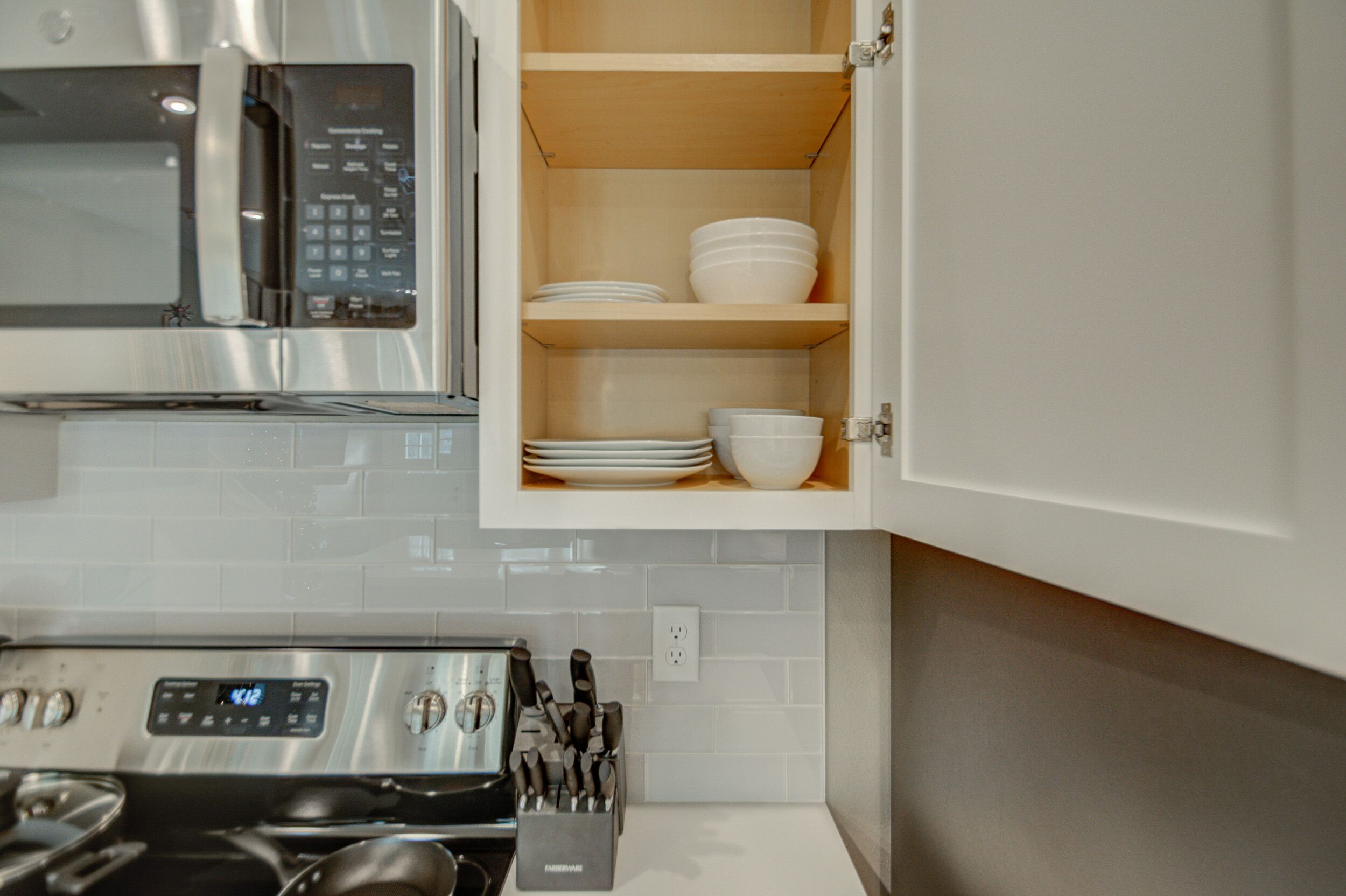 A kitchen with a microwave, stove, and open cabinet with dishes.