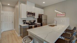 A modern kitchen with white cabinets, a stainless steel refrigerator, a microwave, and a large island with bar stools. - Cozy Houston Getaway in Gated Community (Houston)