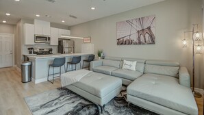 A modern kitchen with a central island, bar stools, a grey sofa, and a ceiling fan. - Cozy Houston Getaway in Gated Community (Houston)
