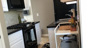 A compact kitchen with white cabinets, a black microwave, a stove, and a refrigerator. - Comfy and Cozy Centrally located in Houston!! (Houston)