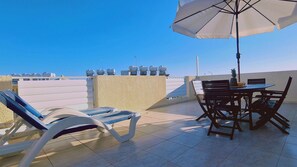 Una terraza en la azotea con una mesa y sillas, una tumbona y un gran paraguas.