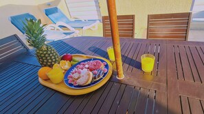 Una mesa de madera con una bandeja de frutas, un vaso de jugo de naranja y una silla de madera.