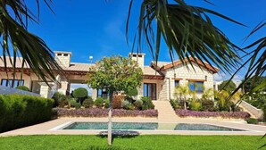 Ein zweistöckiges Haus mit Naturstein-Fassade, einem Swimmingpool und einem gepflegten Garten mit verschiedenen Pflanzen und Blumen.