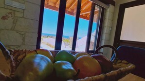 Ein Zimmer mit Steinsturz, einem Fenster mit Meerblick und einem Obstkorb auf einem Tisch.