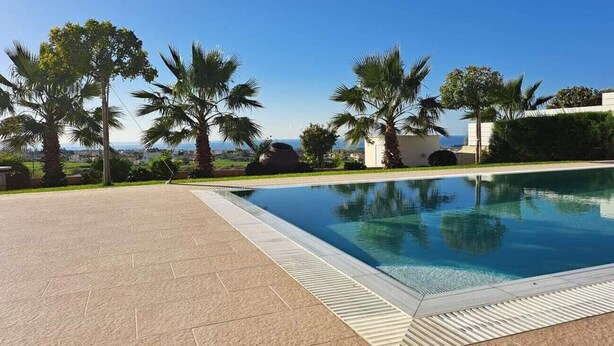 Ein Swimmingpool mit freiem Blick auf das Meer, umgeben von Palmen und einem gepflasterten Weg.