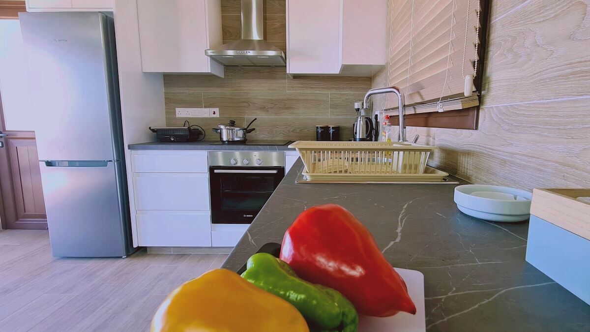 A modern kitchen with a stainless steel refrigerator, oven, and stove. There are three colorful bell peppers on a cutting board.
