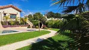 Ein Haus mit einer Steinaußenfassade, einem Swimmingpool und einem gepflegten Garten mit Palmen und Sträuchern.