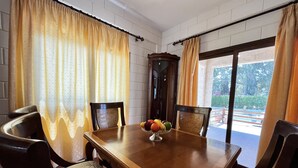 Un comedor con una mesa y sillas de madera, un frutero y cortinas.