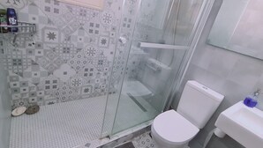 Kylpyhuoneessa on kuvioitu laattalattia, wc-istuin, pesuallas, jossa on saippuanannostelija, sekä suihkutila, jonka erottaa muusta tilasta lasiovi.