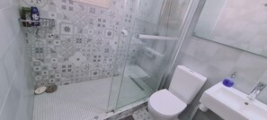 Kylpyhuoneessa on kuvioitu laattalattia, wc-istuin, pesuallas, jossa on saippuanannostelija, sekä suihkutila, jonka erottaa muusta tilasta lasiovi.