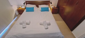 A neatly made bed with white linens and blue pillows, two bedside tables with lamps, and a wooden wardrobe. - STAY Panorama - Kamelia Villa (Peyia)