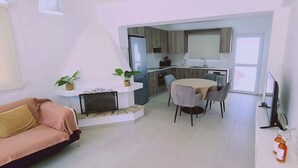 Un saló modern amb un sofà, una llar de foc, una zona de menjador amb taula i cadires, i una cuina al fons.