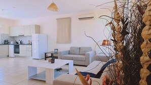 Eine moderne Küche mit weißen Schränken, einem weißen Kühlschrank und einer Kaffeemaschine. Im Wohnbereich befindet sich ein beiges Sofa und ein weißer Couchtisch.
