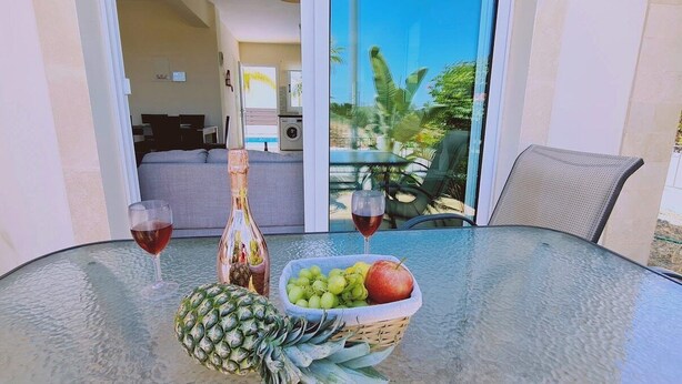 Ein Glastisch mit einer Ananas, einer Flasche, einer Obstschale und zwei Gläsern Rotwein.