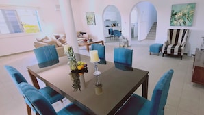Een ruime woonkamer met een eettafel, blauwe stoelen, een keuken achtergrond en een trap naar een ander niveau.