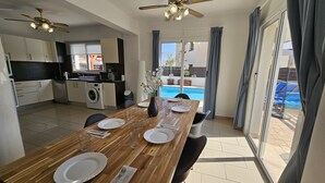 A modern kitchen with a washing machine, dining table set for four with plates, glasses, and cutlery. - STAY Villa Anemone (Protaras)