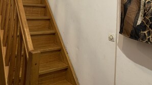 A wooden staircase with a handrail, leading to a white wall with a switch and a framed picture. - Small room near Belgium (Halluin)