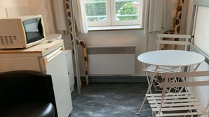 A compact room with a small table and chairs, a desk with a computer, a radiator, and a window with curtains. - Small room near Belgium (Halluin)