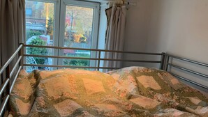 A bedroom with a large bed, a window with curtains, and a view of the outside. - Small room near Belgium (Halluin)