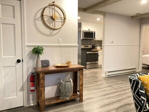 A modern kitchen with white cabinets, a microwave, and a stove. There is a wooden console table with a plant and a bowl on it.