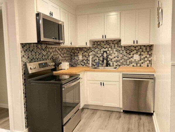 A modern kitchen with white cabinets, a microwave, a stove, a dishwasher, and a sink.