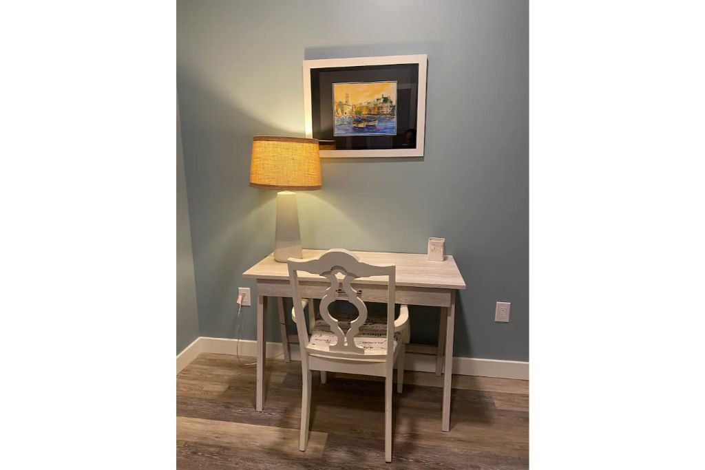 Un petit coin repas avec une table et une chaise, une lampe et un tableau encadré au mur.