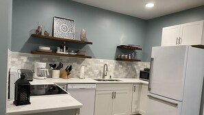 Una cocina moderna con armarios blancos, microondas integrado, pileta de acero inoxidable y piso de madera.